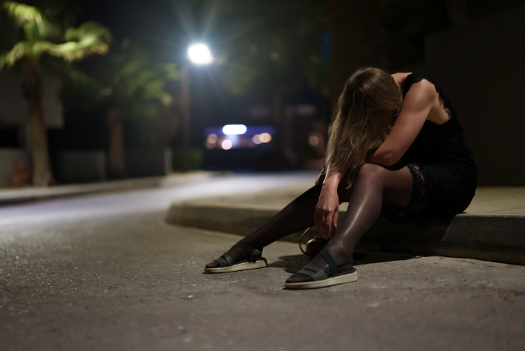 Drunk woman sits on a street at night.