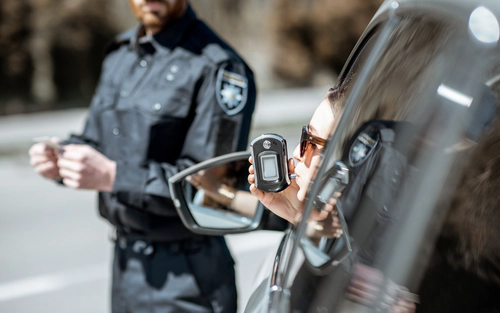 Woman taking breathalyzer test with police on-looking